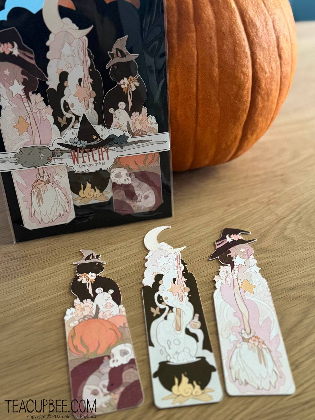 Halloween-themed bookmarks with illustrations of witches and cats on a wooden surface with a pumpkin.