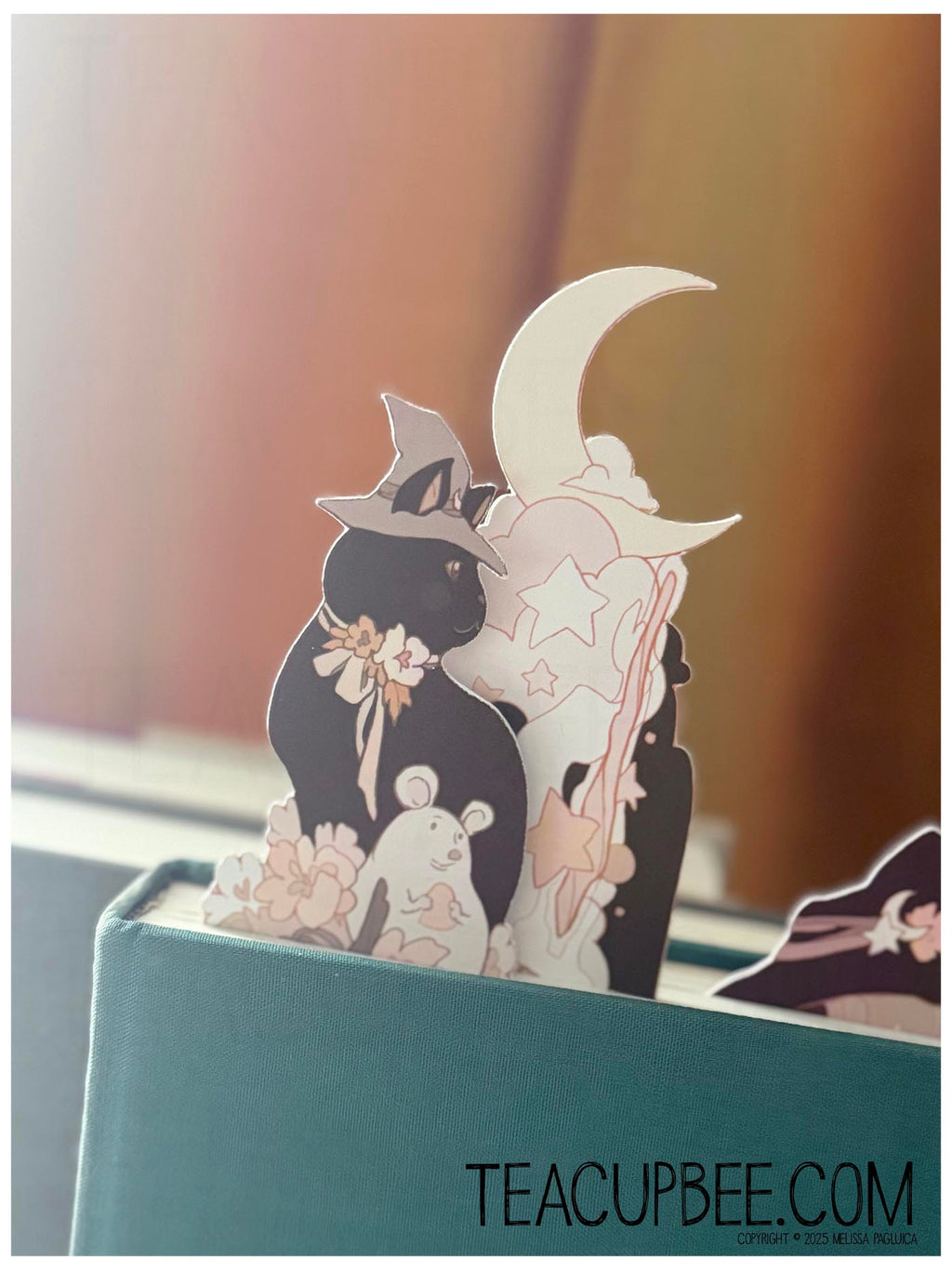 Decorative cutout of a witch, moon, and cat on a teal book with 'TeacupBee.com' branding.