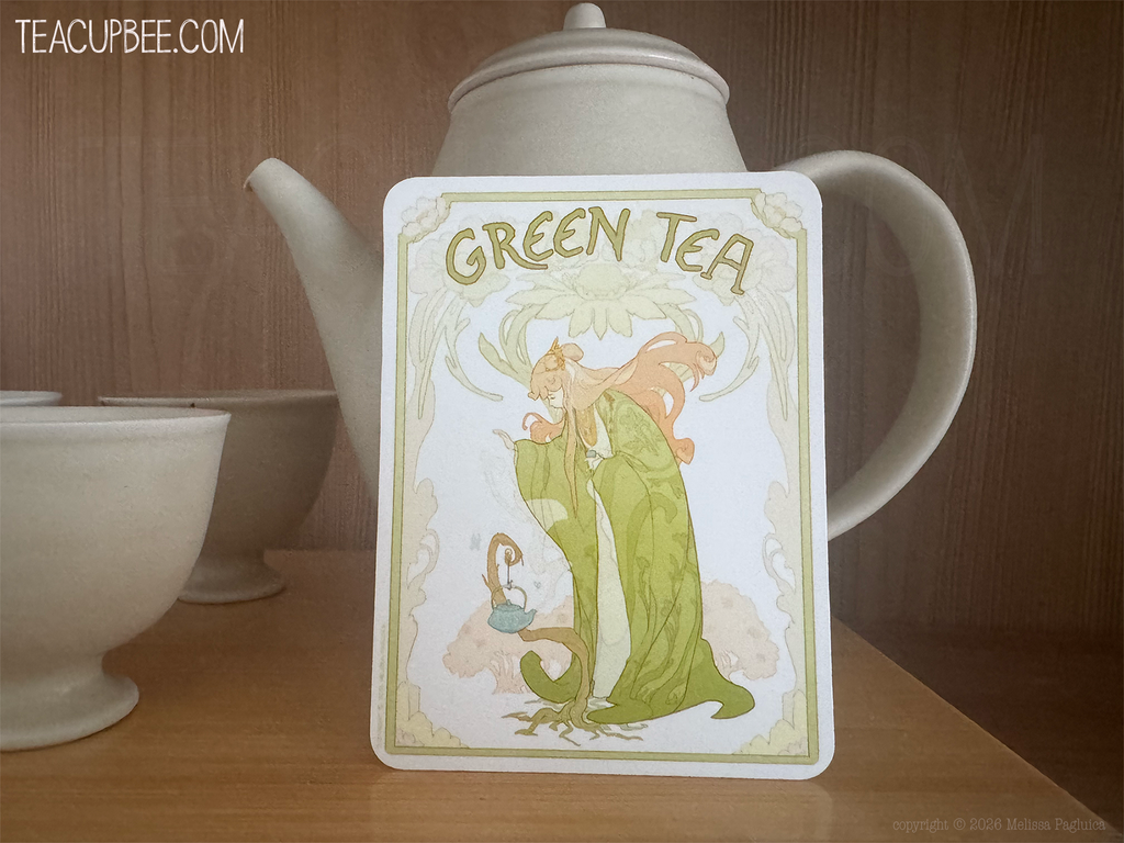 A square tea tin labeled 'GREEN TEA' with an Art Nouveau illustration of a woman in a green dress, standing on a wooden surface in front of a white ceramic teapot and bowls. The watermark 'TEACUPBEE.