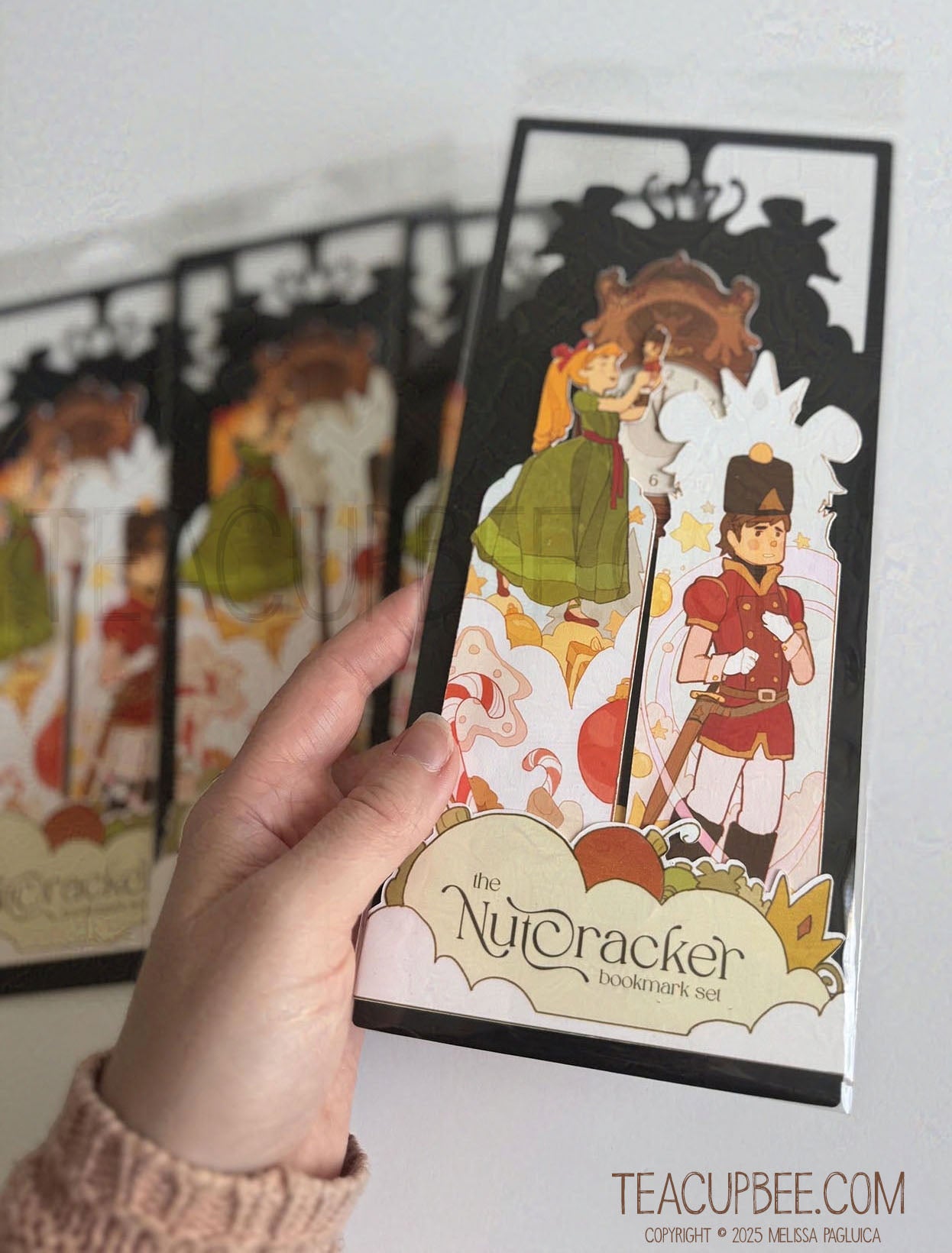 Hand holding a Nutcracker-themed bookmark with other bookmarks in the background.